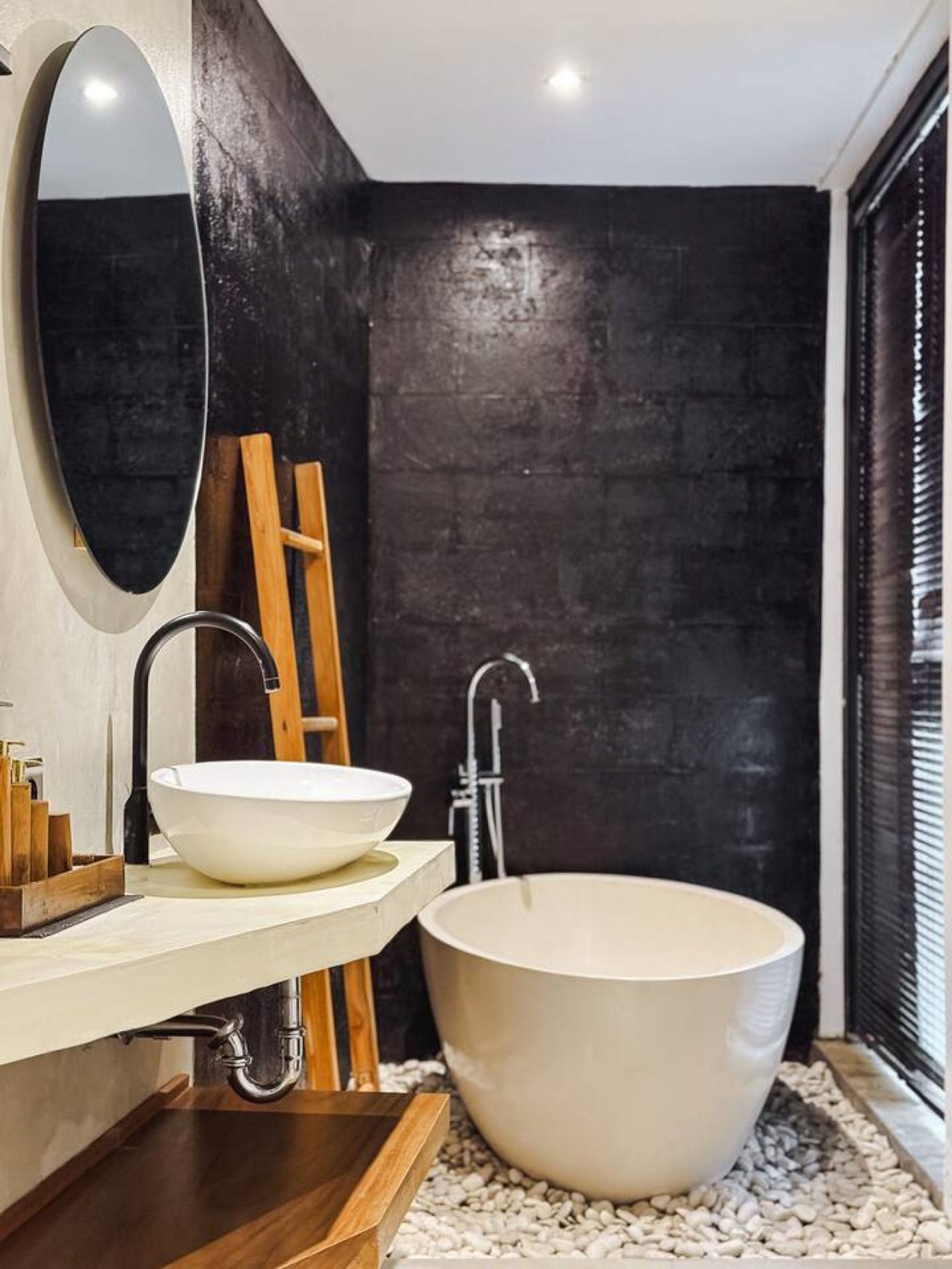Freestanding soaking tub against dark stone beside a teak ladder, open to the garden