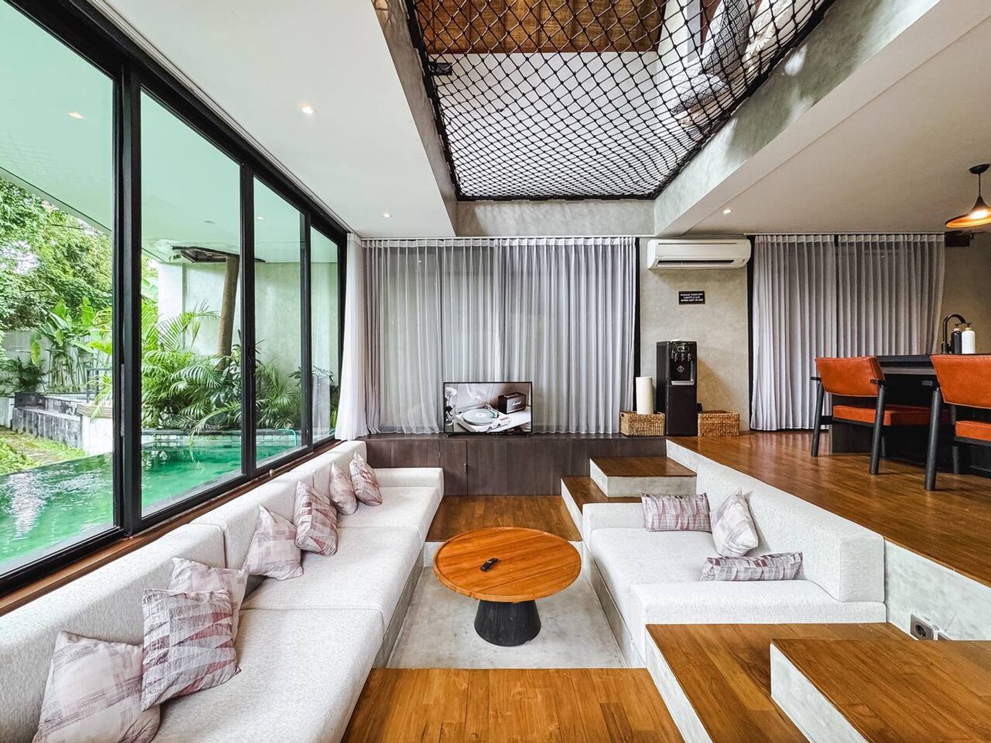 Sunken living room with pale sofas facing floor-to-ceiling glass and the pool